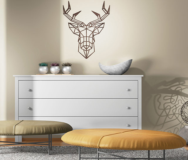 A white dresser with yellow ottomans and a deer head on the wall.